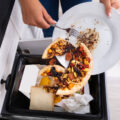 Close-up Of A Person Throwing Pepperoni Pizza On Plate In Dustbin